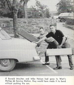 Ronald and Mike pushing a car with their trombone cases in hand