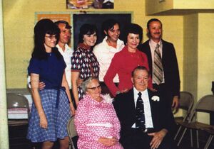 an older couple are seated with five adult children standing behind them.