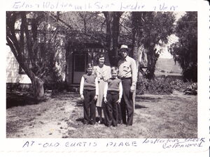 A man and a woman stand with their two sons, about ages six and seven in front of a house.